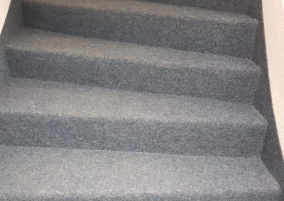 Détail des marches et contremarches couvertes d’une moquette grise à la finition impeccable.
