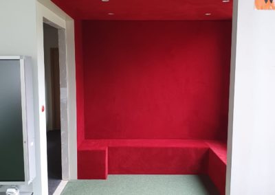 Espace lecture d’une école avec murs et banquette entièrement habillés en moquette rouge pour un confort acoustique et visuel.