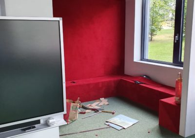 Banquette sur mesure recouverte de moquette rouge dans un coin lecture scolaire, finitions impeccables.