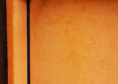 Intérieur d’une malle restaurée avec un habillage en cuir orange et finitions décoratives.