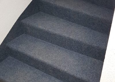 Escalier entièrement recouvert de moquette grise pour un revêtement antidérapant et confortable.