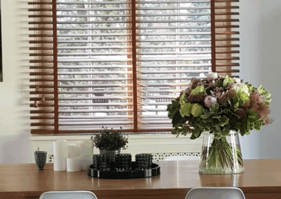 Stores à lamelles en bois installés sur mesure dans une cuisine moderne avec table en bois et décoration florale.