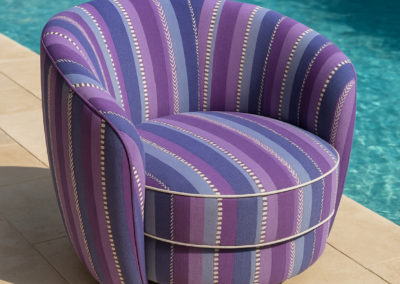 Fauteuil rond design tapissé d’un tissu rayé violet, bleu et lilas, création sur mesure Rho Deco.